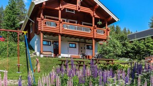A log cabin with a balcony, surrounded by a garden with purple flowers.
