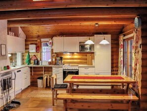 A cozy cabin-style kitchen with wooden walls, a dining table, and basic appliances.