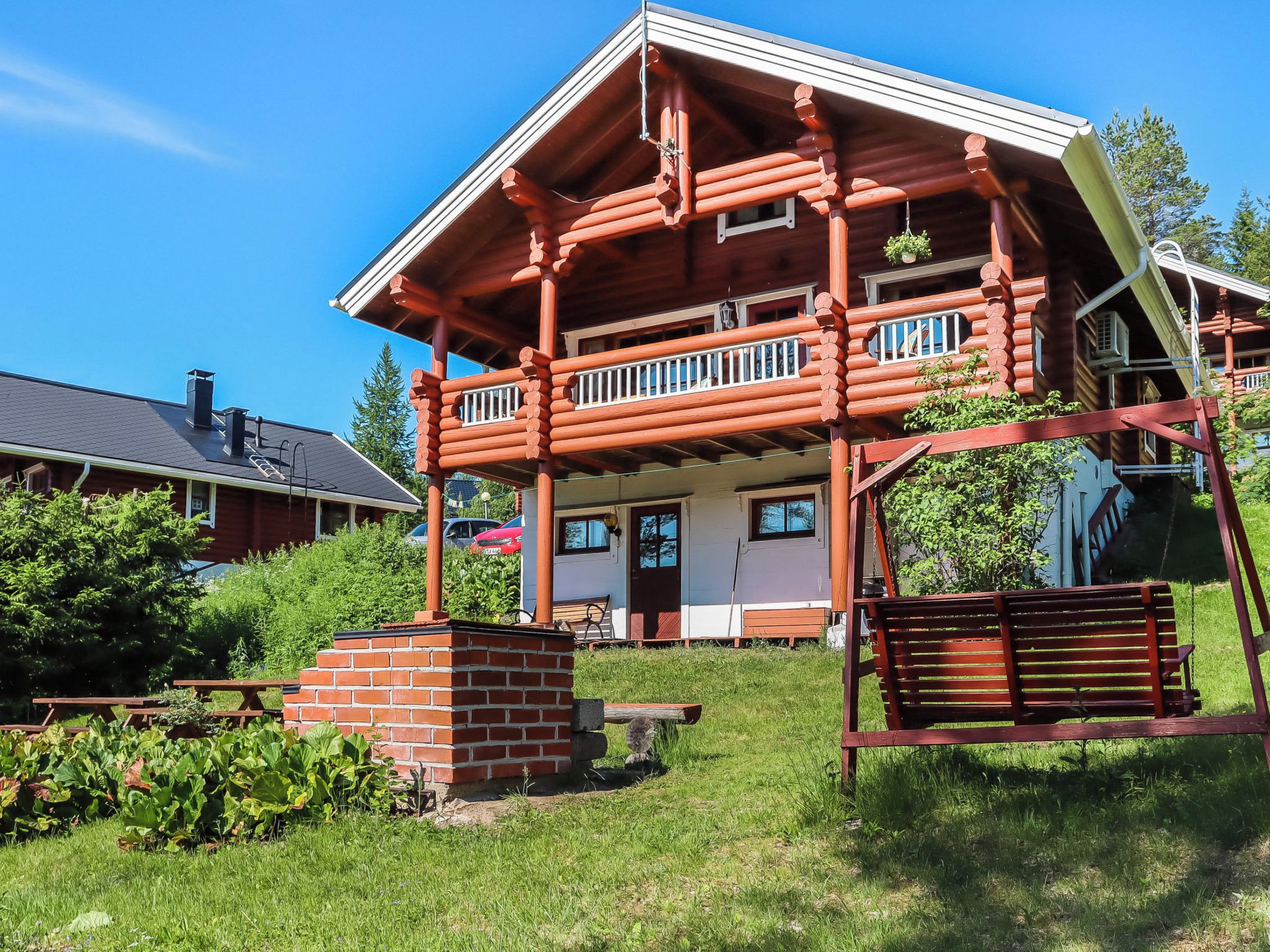 A two-story log cabin with a balcony, a brick fireplace, and a swing set.