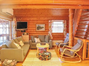 L’intérieur d’un chalet chaleureux, avec un canapé, un fauteuil et un téléviseur fixés à un mur en bois.