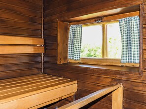 A wooden cabin interior with a bench, a window with checkered curtains, and a view of greenery outside.