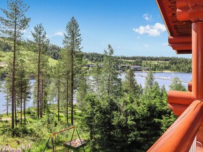 Blick auf ein Seeufer mit Holzterrasse, Bäumen und blauem Himmel.