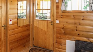 A wooden cabin interior with a wooden door, a window with a view, and a doormat.