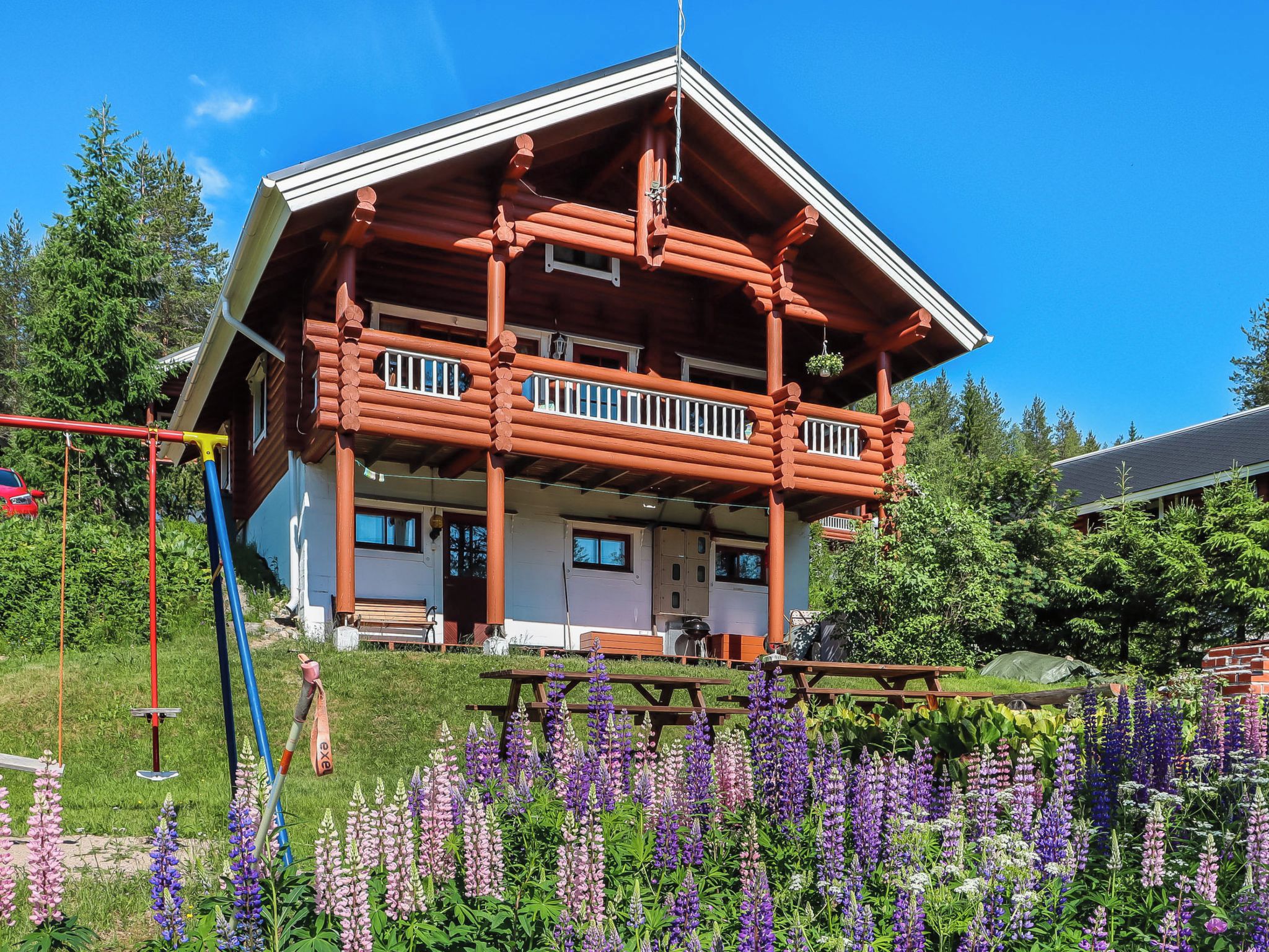 A log cabin with a balcony, surrounded by a garden with purple flowers.