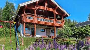 A log cabin with a balcony, surrounded by a garden with purple flowers.