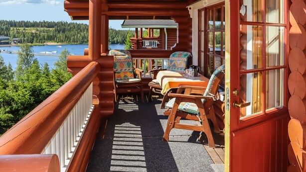 A wooden deck with a view of a lake, furnished with chairs and a table, and a door with a window.