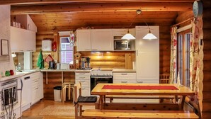 A cozy cabin-style kitchen with wooden cabinets, a dining table, and a hanging light fixture.