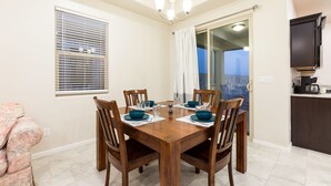 A dining area with a wooden table and chairs, a chandelier, a window with blinds, a sliding glass door, and a kitchen area with dark cabinets. - Relaxing Oasis Near White Sands National Monument (Las Cruces)