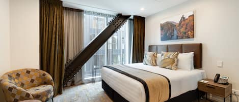 A hotel room with a large bed, a chair, a nightstand, and a staircase leading to a balcony.