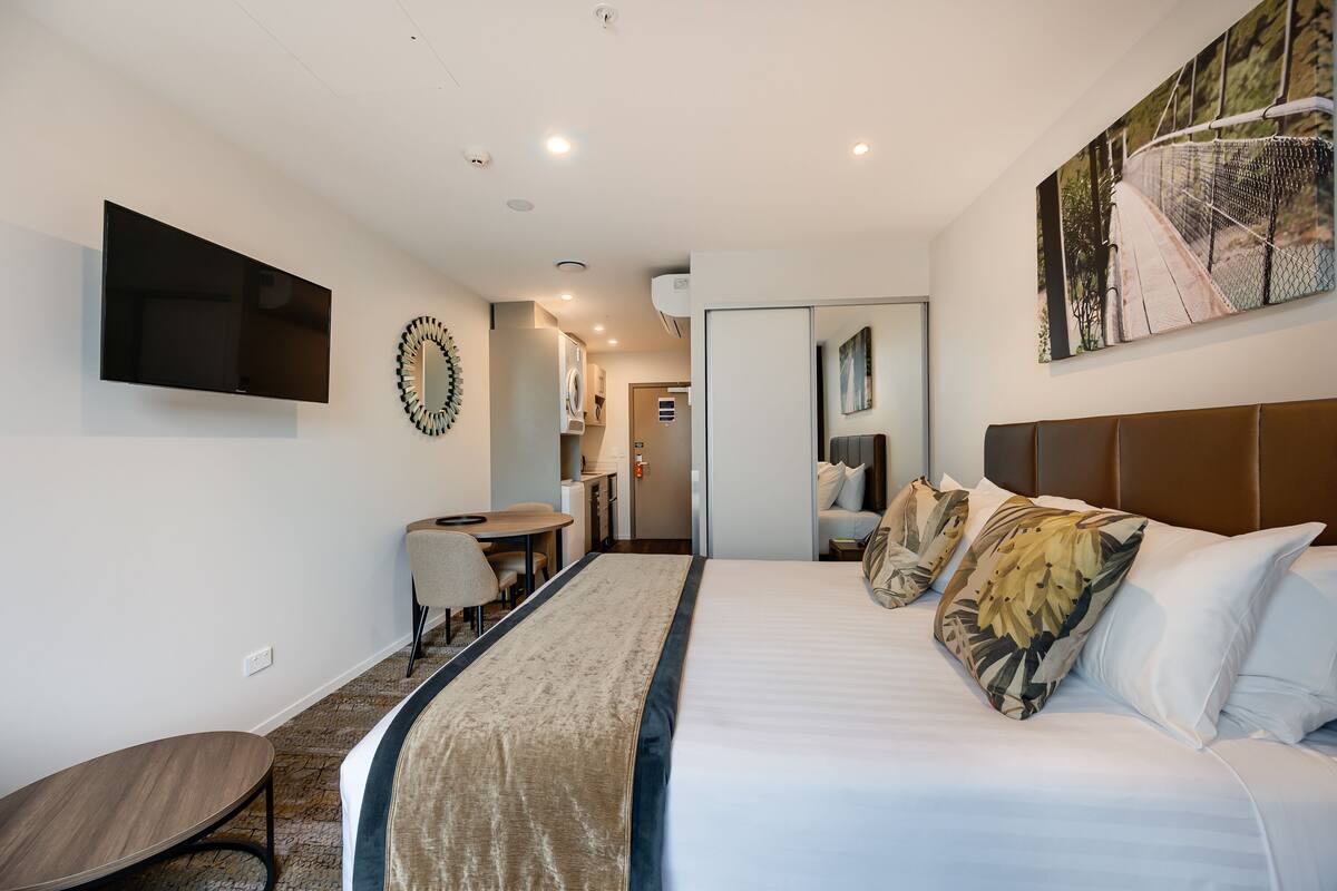 Ein modernes Hotelzimmer mit einem großen Bett, einem Flachbildfernseher, einem Essbereich und einem durch eine offene Tür einsehbarer Badezimmer.