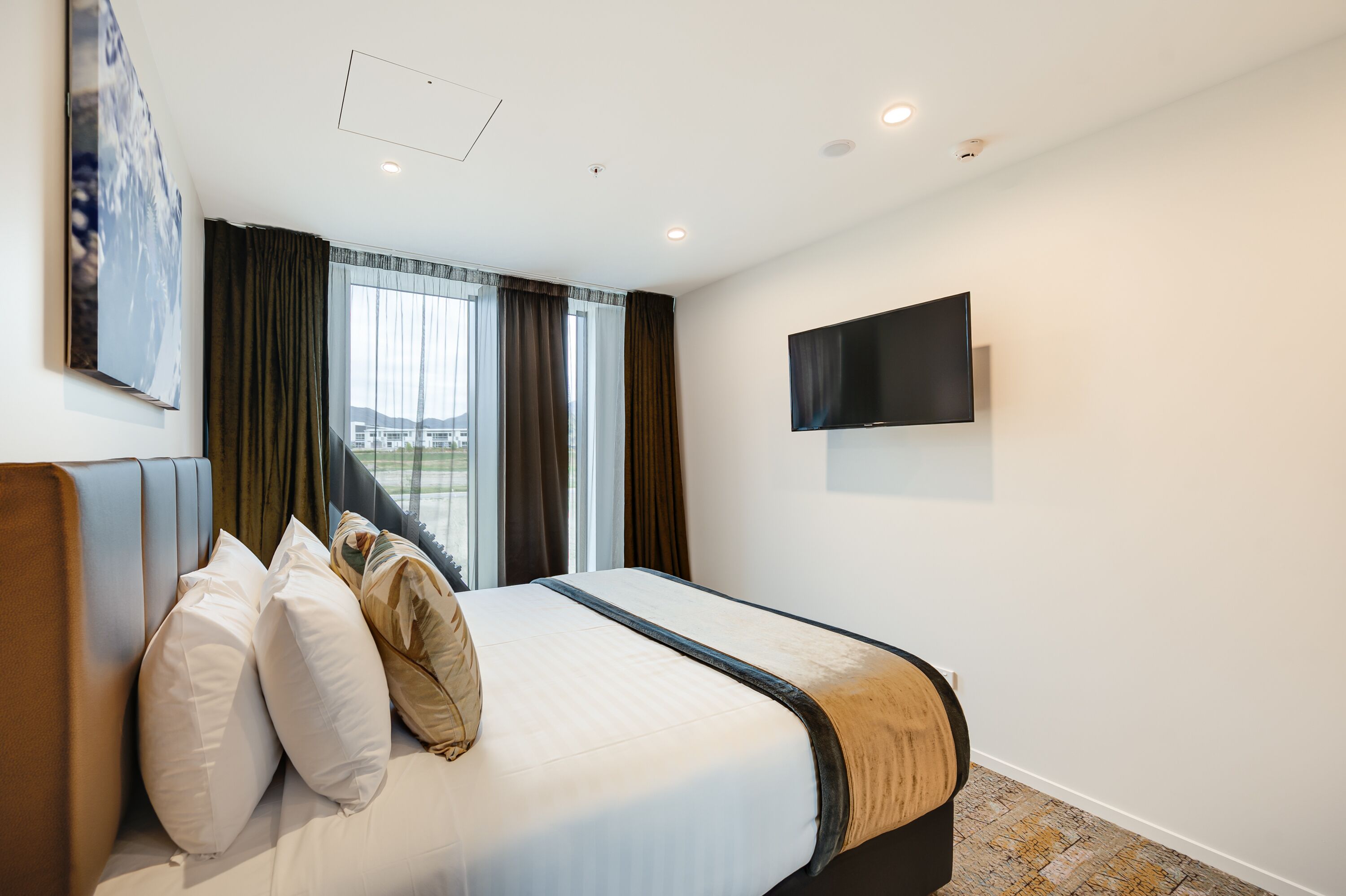 A hotel room with a bed, a flat-screen TV mounted on the wall, and a window with curtains.