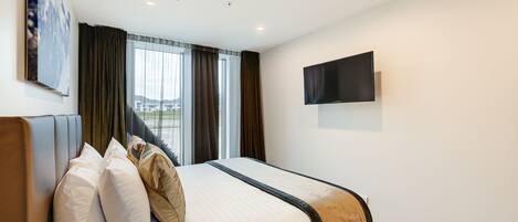 Ein Hotelzimmer mit Bett, einem flachbildfernseher an der Wand und einem Fenster mit Vorhängen.