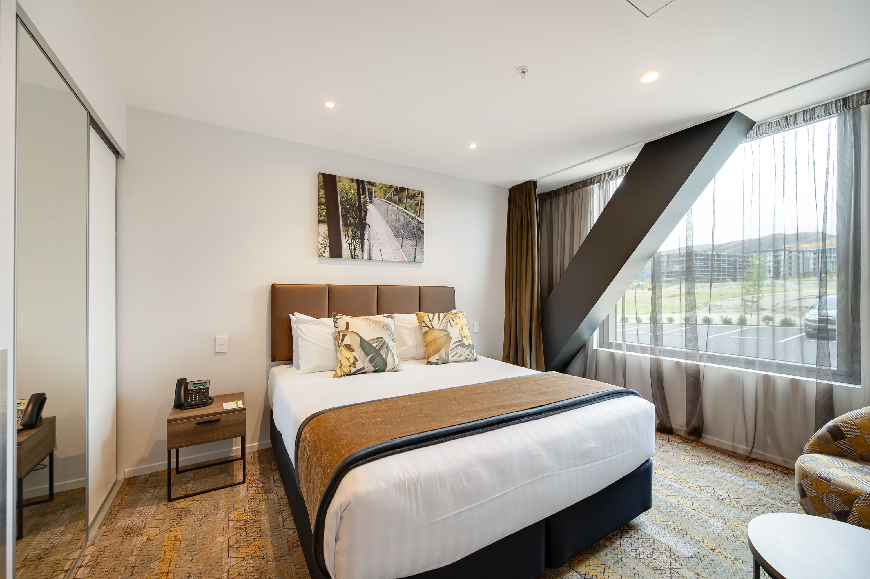 Habitación de hotel con una cama grande, una mesita de noche con un teléfono, una ventana con cortinas y un cuadro en la pared.