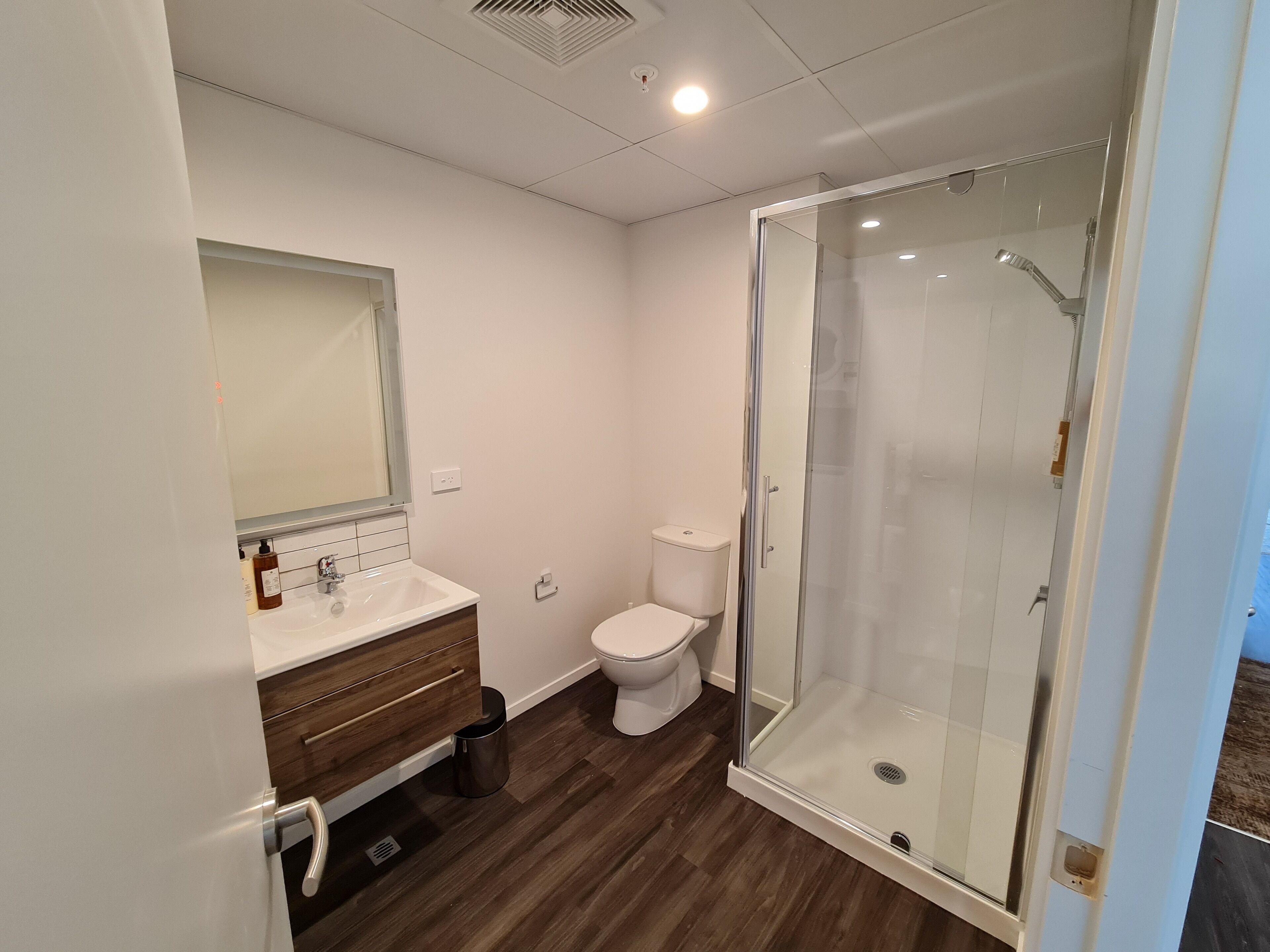 A modern bathroom with a glass-enclosed shower, a white toilet, and a wooden vanity.