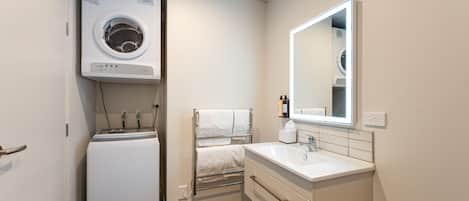 Un baño pequeño con lavadora integrada, un lavabo con espejo y un perchero para toallas.