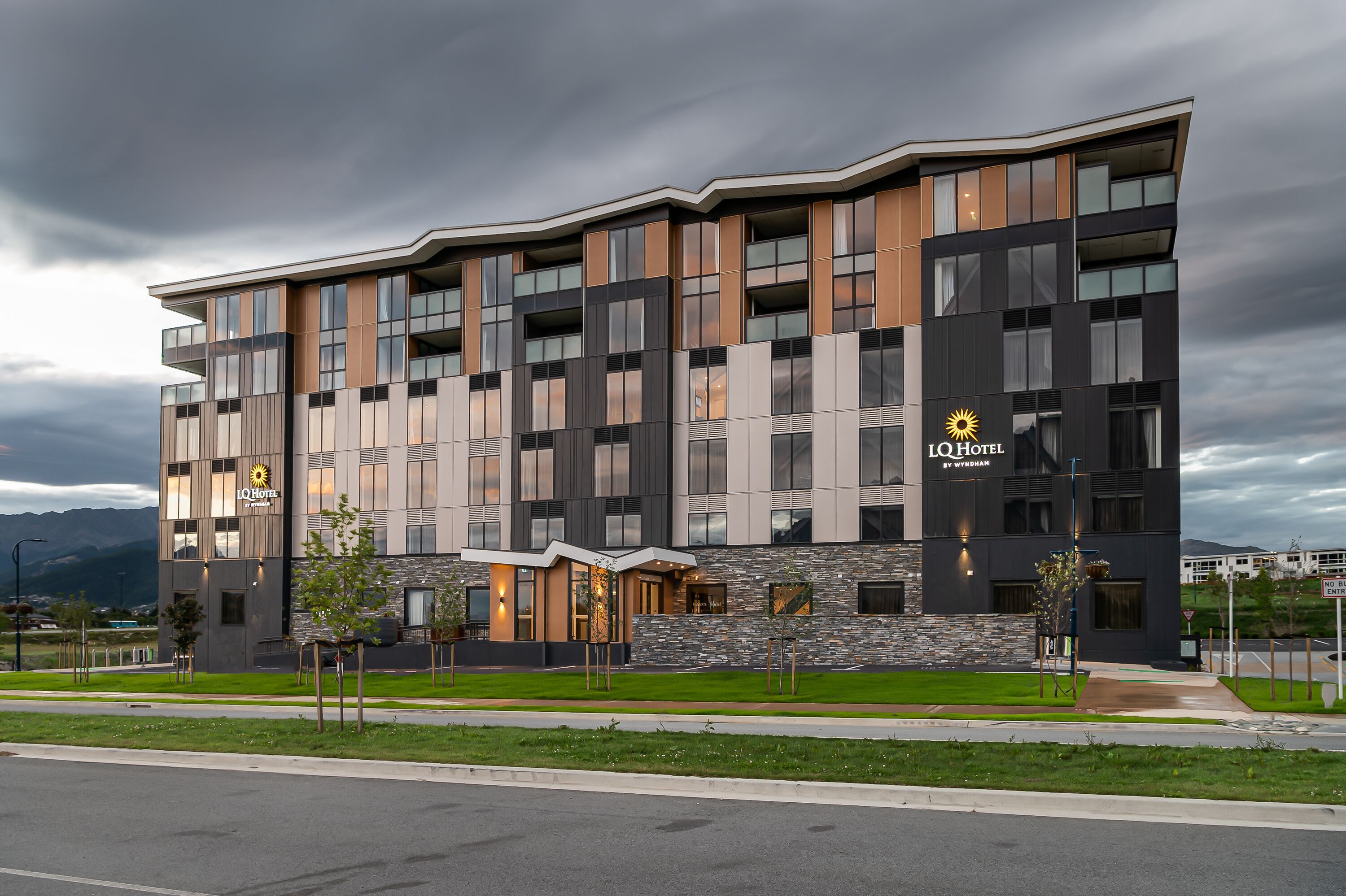 A modern hotel with a flat roof, multiple balconies, and a stone facade.
