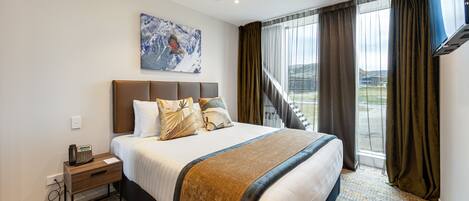Een hotelkamer met een groot bed, een nachtkastje met een telefoon, een schilderij aan de muur en uitzicht op het omliggende landschap door het raam.