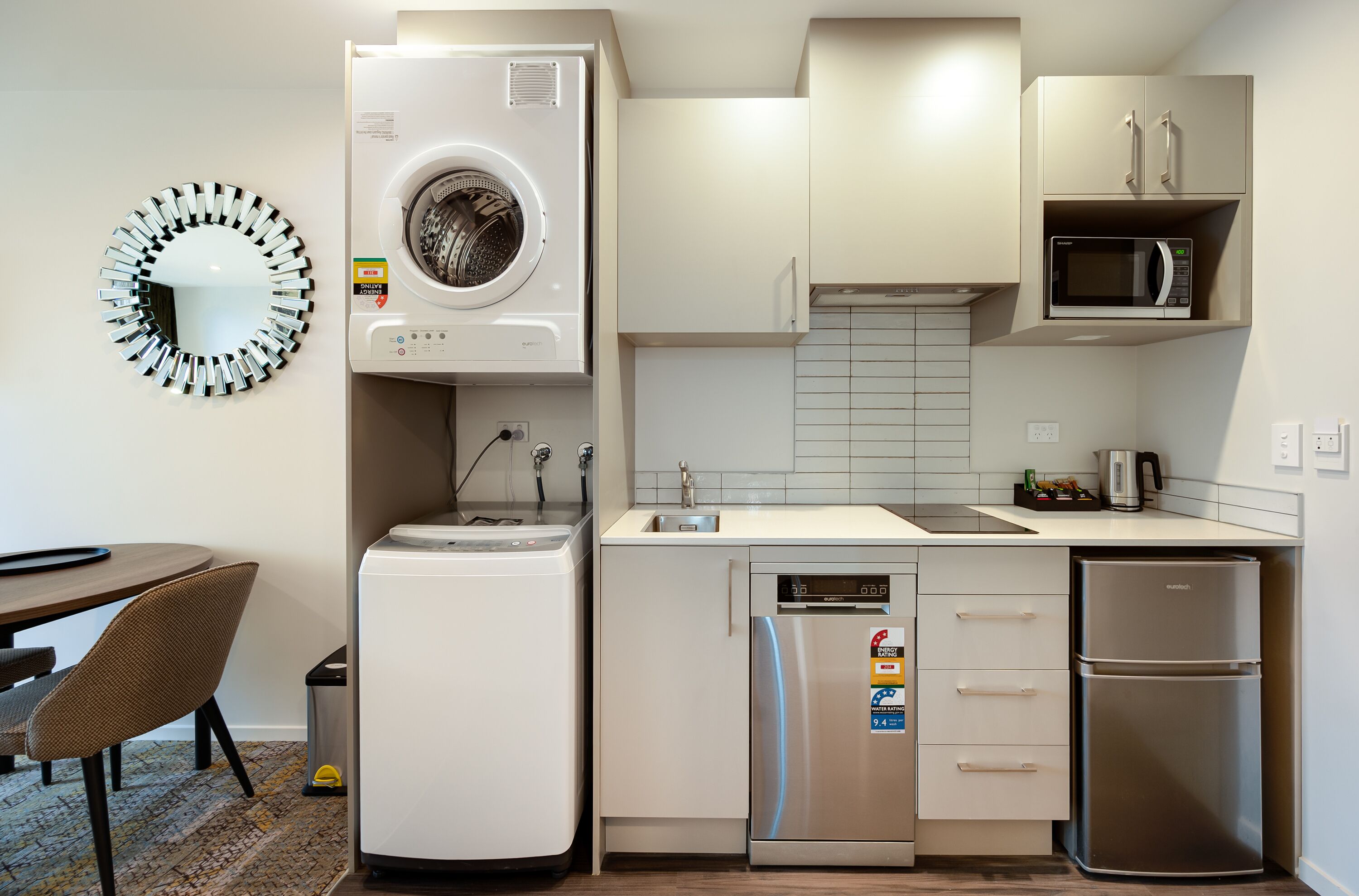 Cocina compacta con lavadora, microondas, refrigerador y comedor con una silla y mesa.