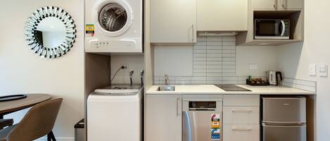 Cocina compacta con lavadora, microondas, refrigerador y comedor con una silla y mesa.