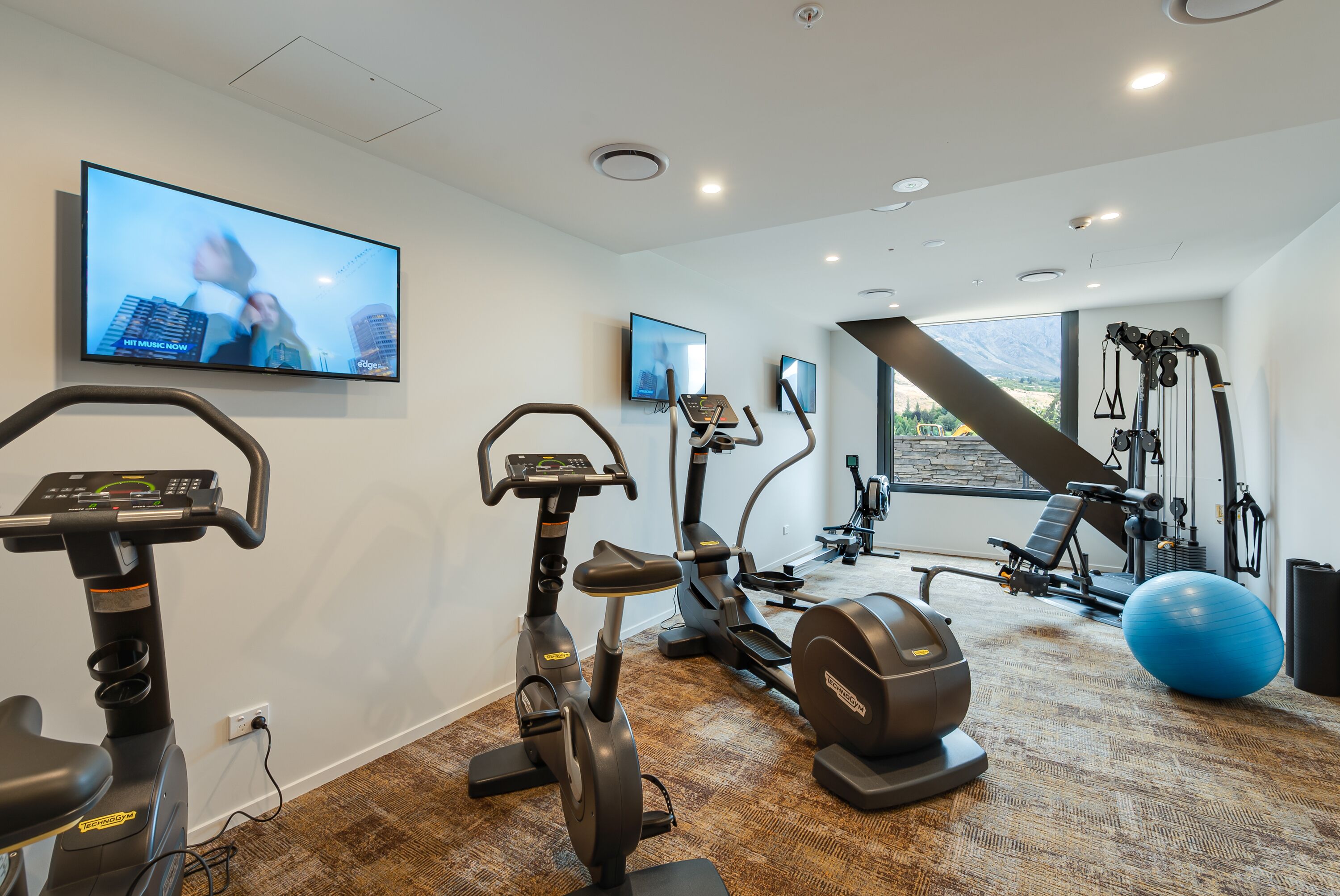 Un gimnasio en casa con equipo de ejercicio, un televisor y un ventanal grande.