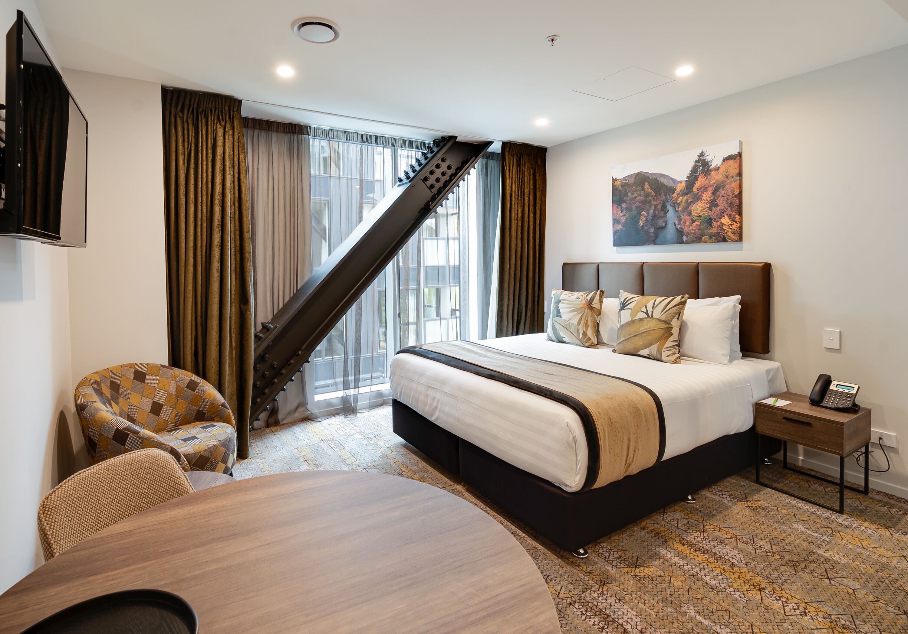 A hotel room with a bed, a desk, a chair, a staircase, and a painting on the wall.
