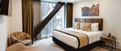 A hotel room with a bed, a desk, a chair, a staircase, and a painting on the wall.