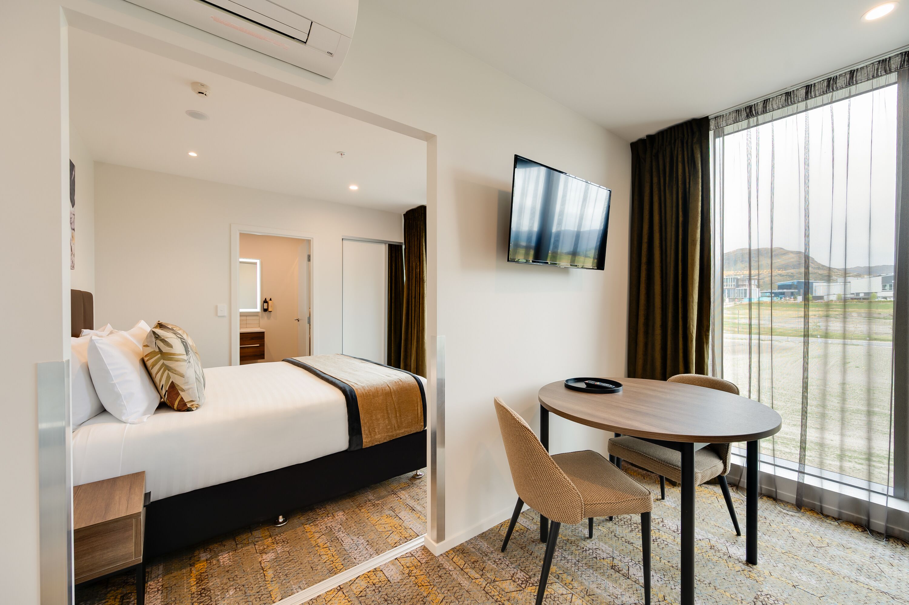 A hotel room with a bed, a desk, a chair, a TV, and a large window with a view.