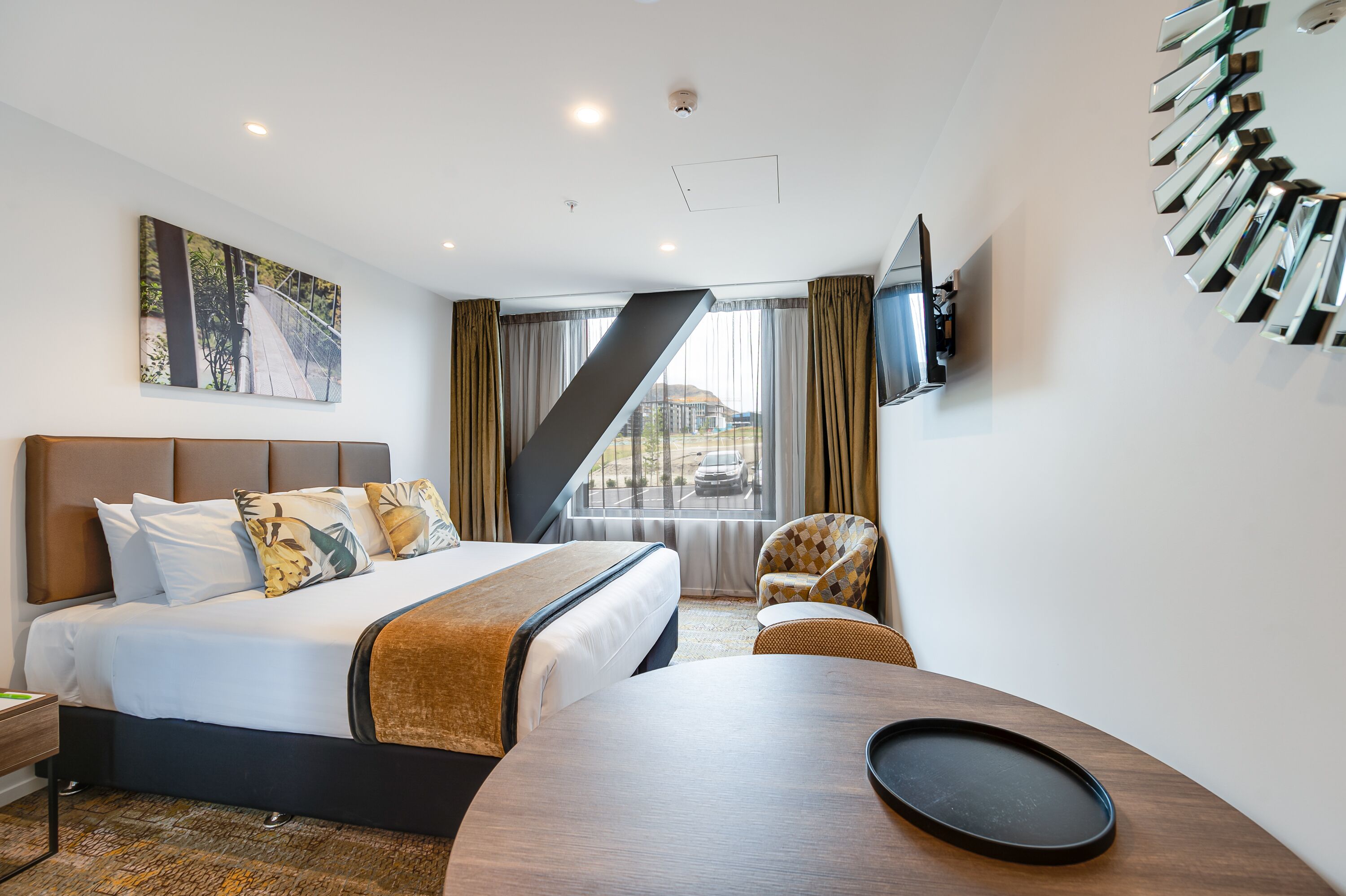 A hotel room with a bed, a desk, a chair, a TV, and a window with curtains.