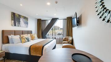 A hotel room with a bed, a desk, a chair, a TV, and a window with curtains.