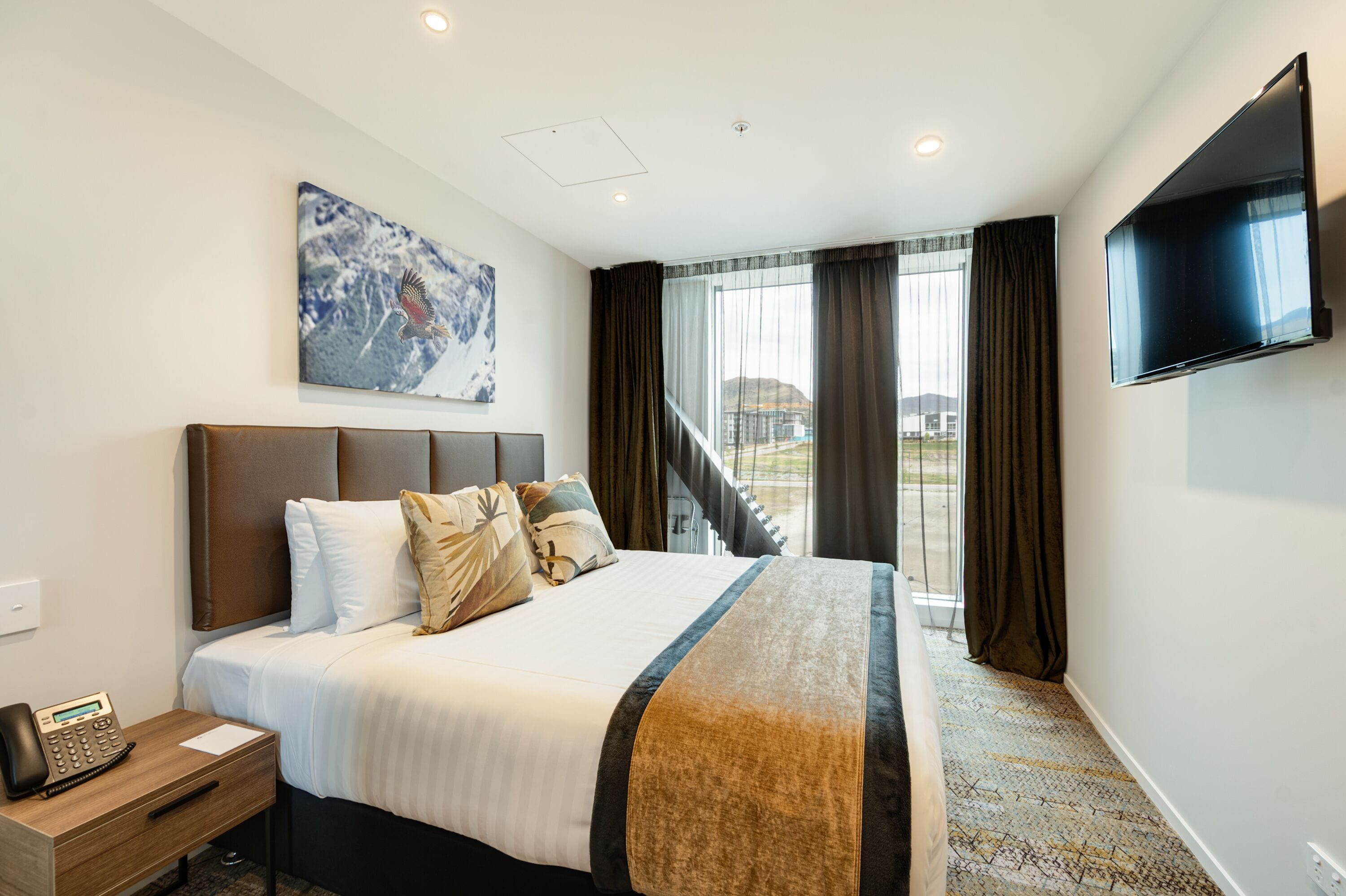 A hotel room with a large bed, a flat-screen TV, a telephone, and a painting on the wall.