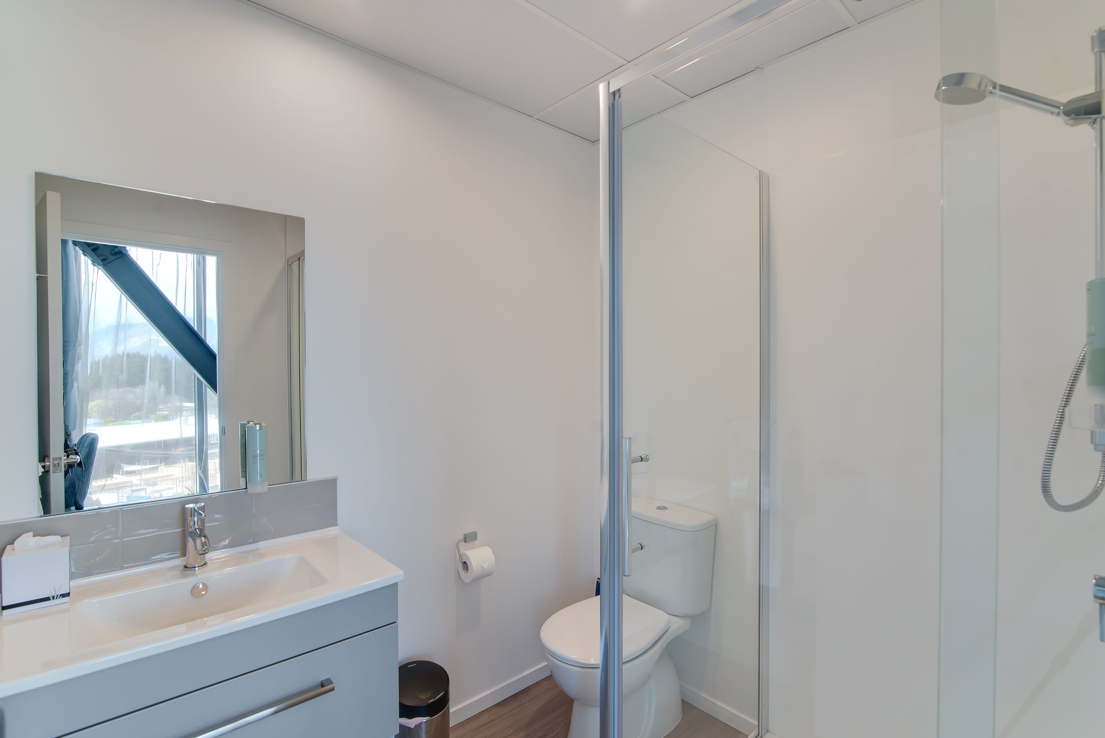 Et moderne badeværelse med et glasbadeværelse, en hvid vask og et toilet.