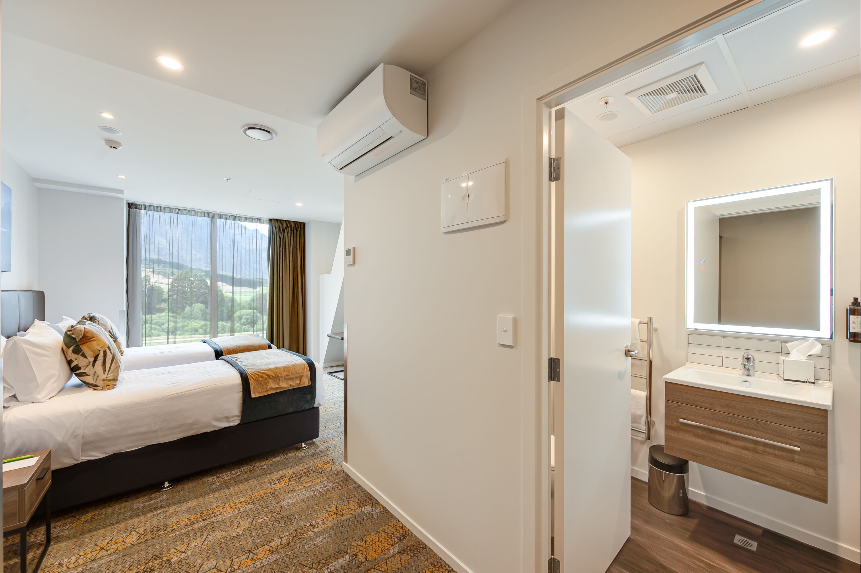 A hotel room with a bed, a bathroom with a mirror and sink, and a window with curtains.