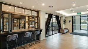Un espace bar moderne, doté d’une paroi vitrée, de tabourets de bar et d’un coin salon avec un canapé et une petite table.