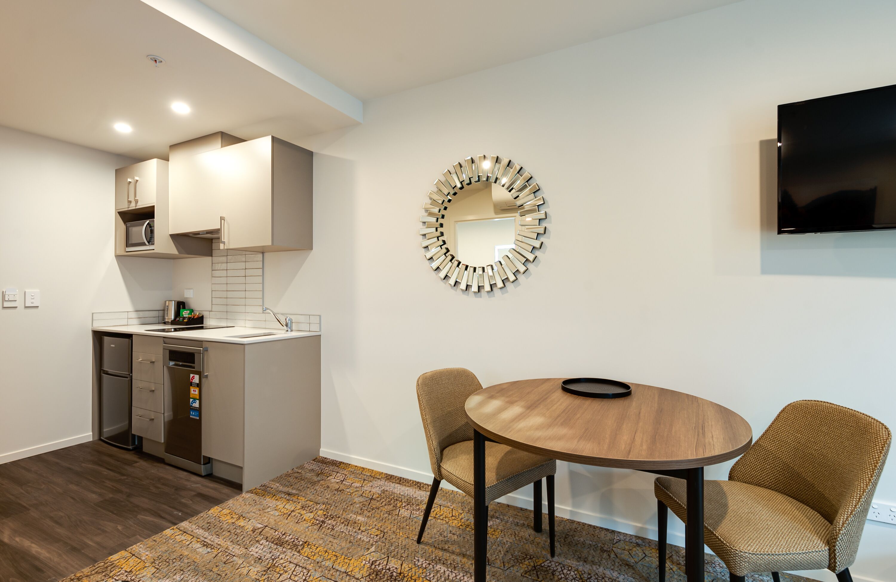 A modern kitchen with built-in appliances, a dining area with two wicker chairs, and a round mirror on the wall.