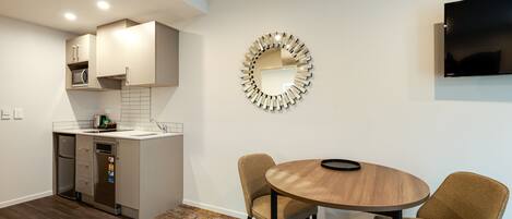 A modern kitchen with built-in appliances, a dining area with two wicker chairs, and a round mirror on the wall.