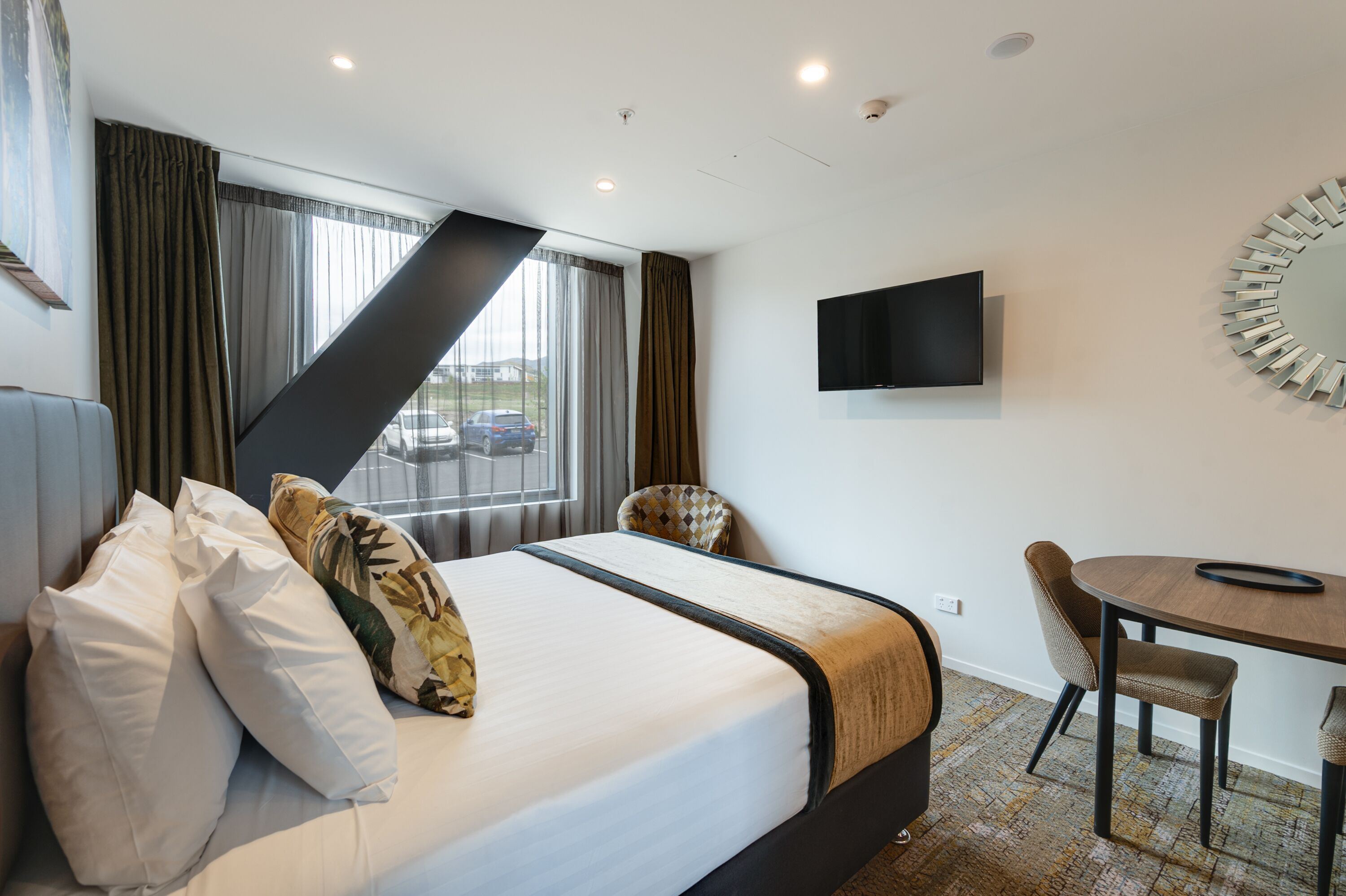 Een hotelkamer met een bed, een bureau, een stoel, een televisie en uitzicht op buiten.