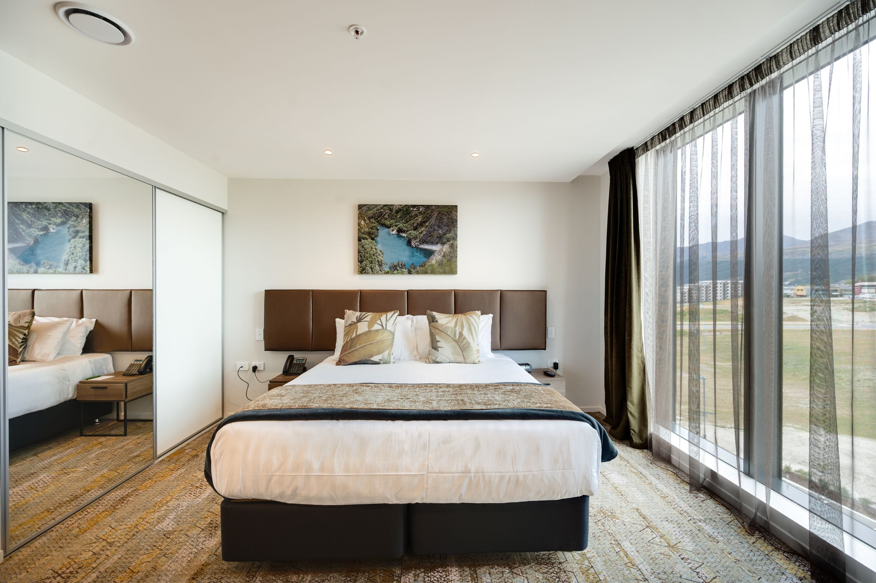 A modern hotel room with a large bed, a view of the outdoors, and a painting on the wall.