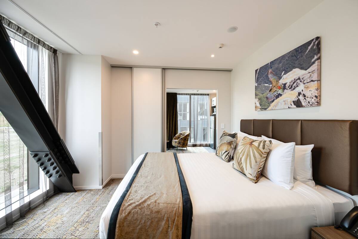 Ein modernes Hotelzimmer mit einem großen Bett, einem Gemälde und Blick durch ein Fenster.