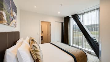 A hotel room with a bed, a large window with curtains, a view of a mountainous landscape, and a door leading to a bathroom.