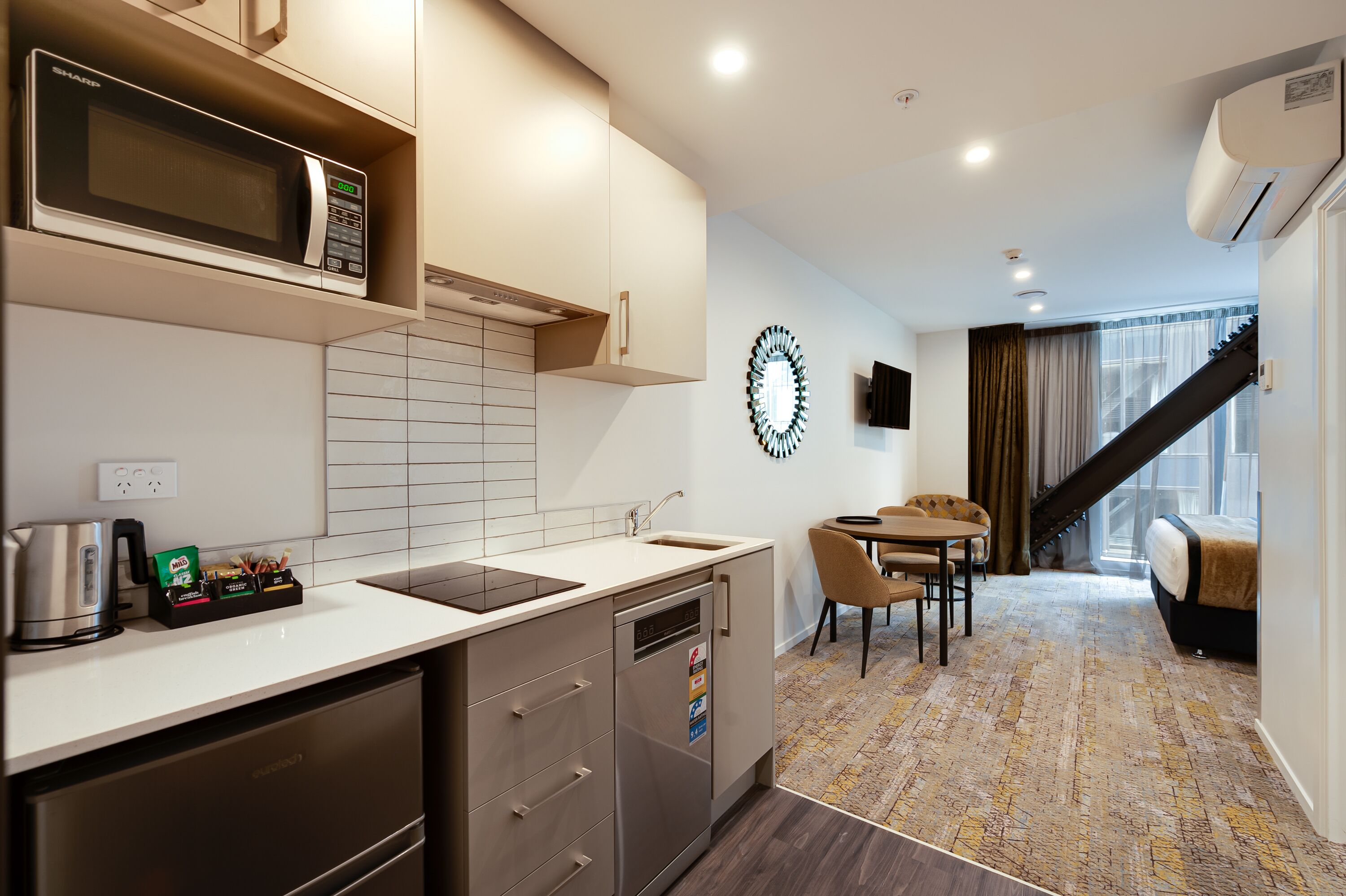 A modern kitchen with a microwave, sink, and dishwasher. There is a dining area with a table and chairs, and a staircase leading to another level.
