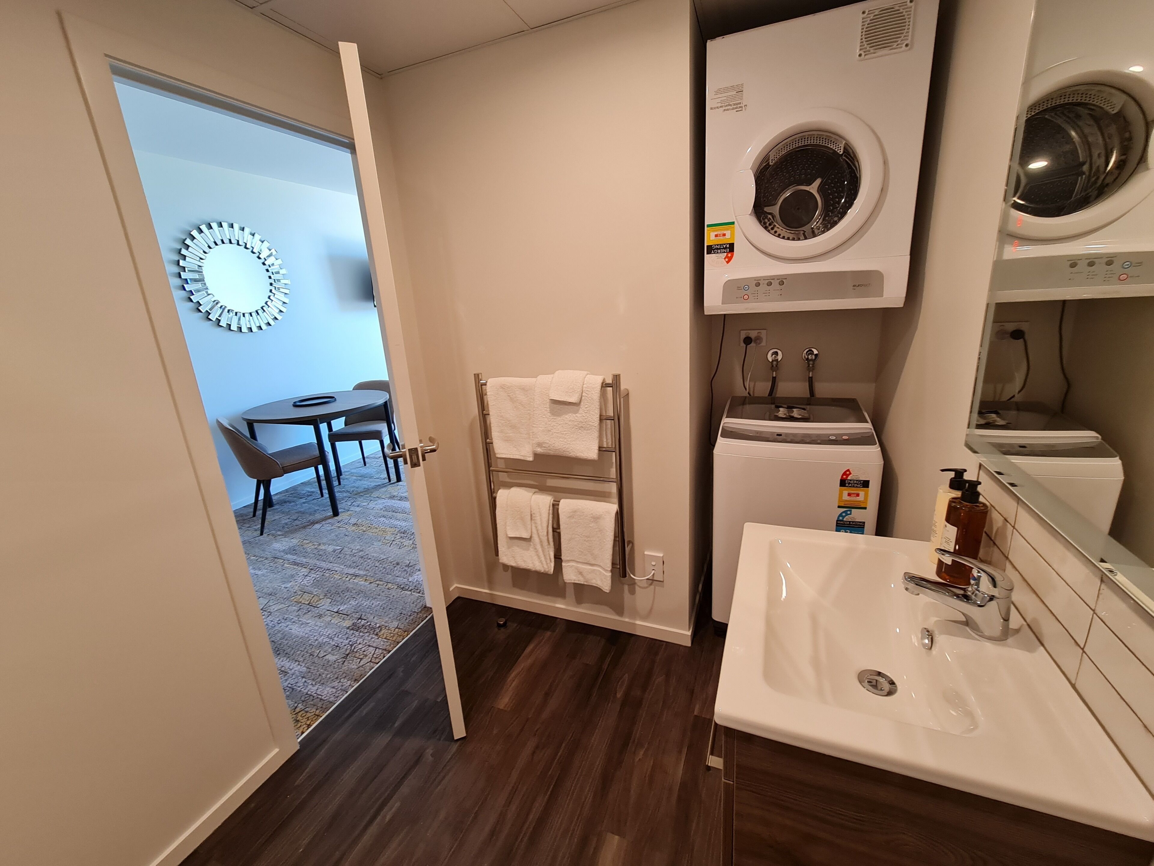 A compact hotel bathroom with a sink, a washing machine, and a mirror.