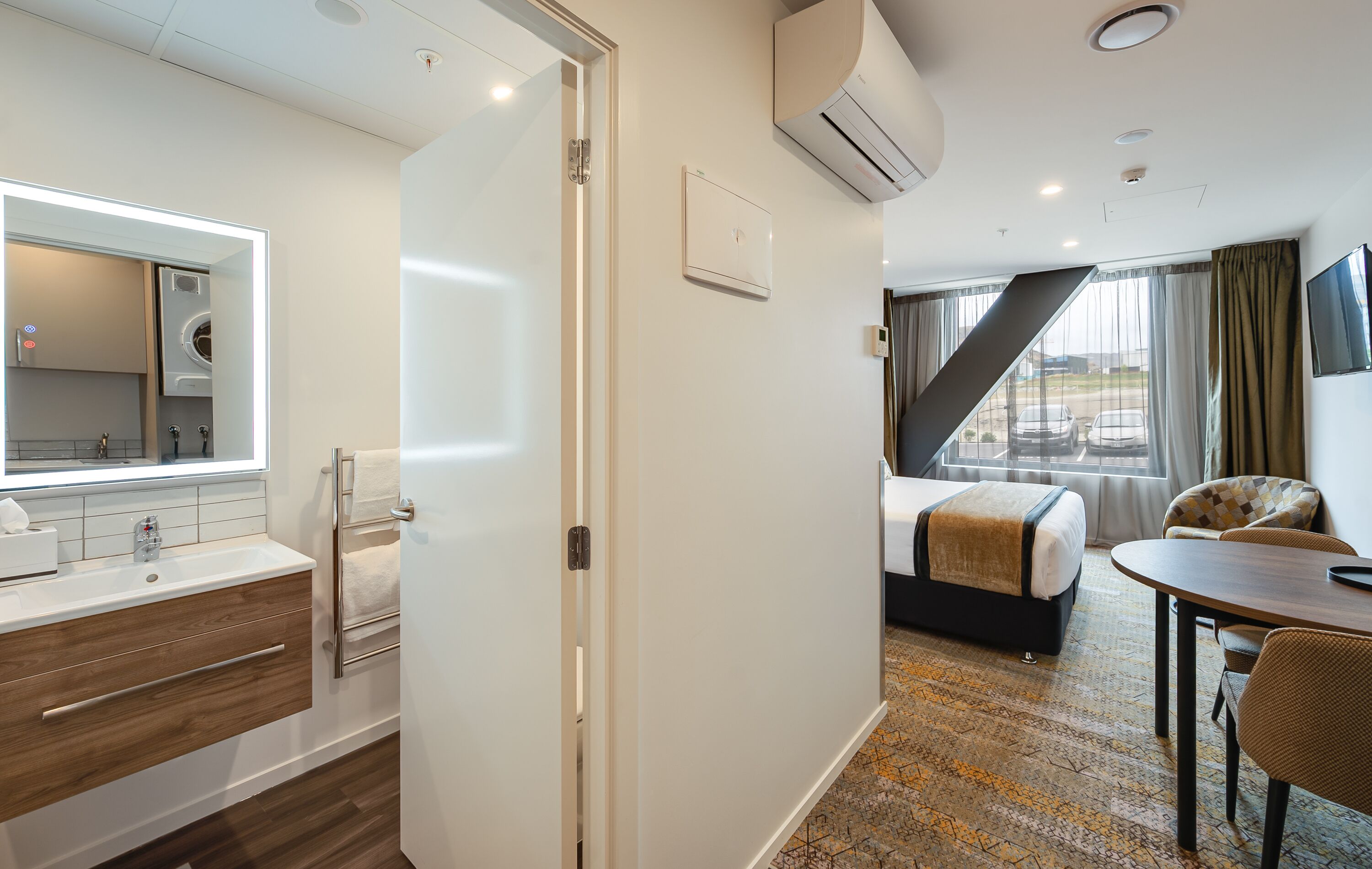 A hotel room with a bathroom, a bed, a desk, and a view of the outside.