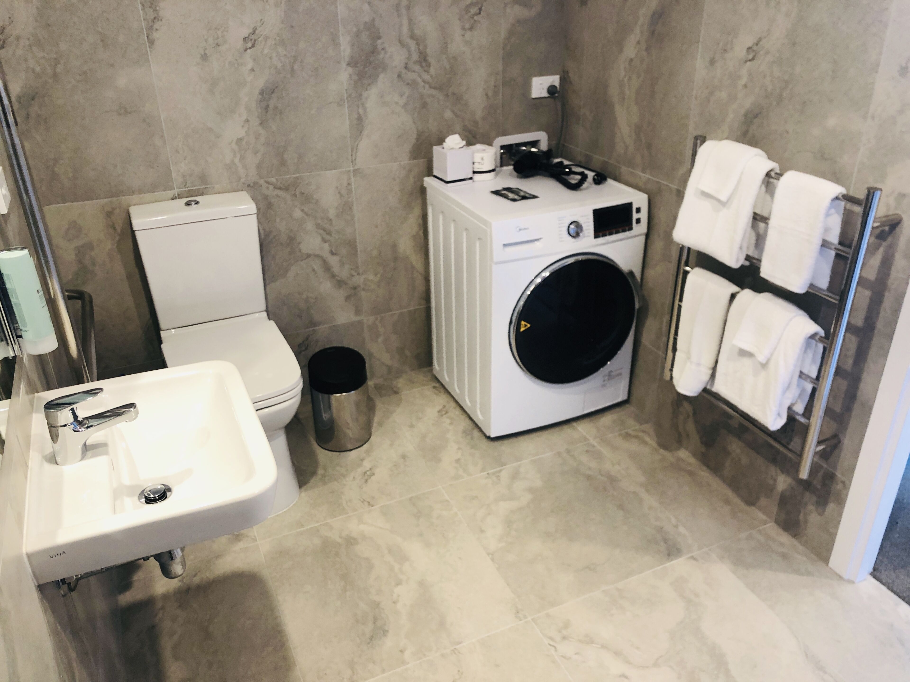 A compact bathroom with a toilet, sink, washing machine, and towel rack.