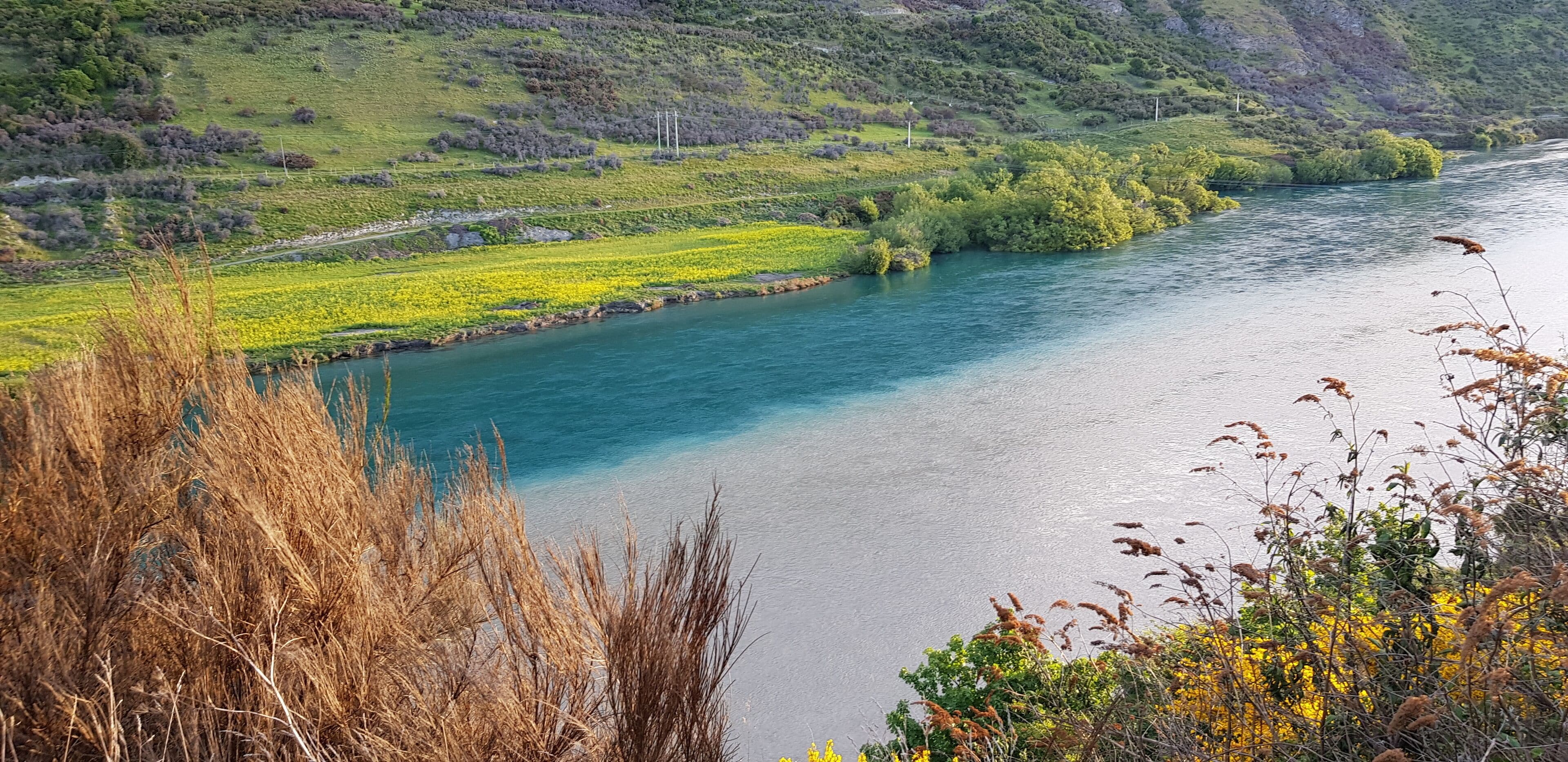 A river flowing through a valley with green fields and hills in the background.