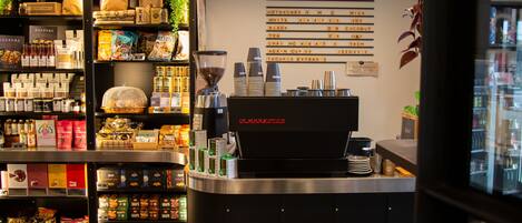 A coffee shop interior with shelves stocked with snacks, a coffee machine, and a menu board.