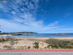 A coastal road with a beach and dunes in the background.