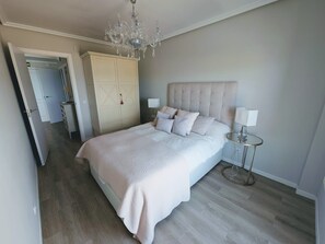 A bedroom with a large bed, a chandelier, a wardrobe, and a bedside table.