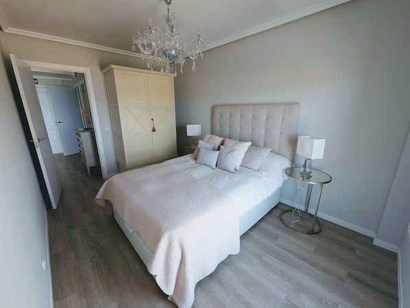 A bedroom with a large bed, a chandelier, a wardrobe, and a bedside table.