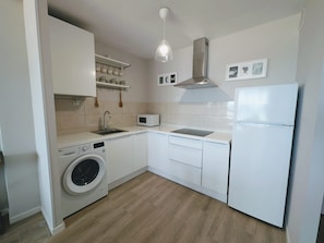 A compact kitchen with a washing machine, microwave, and a refrigerator.