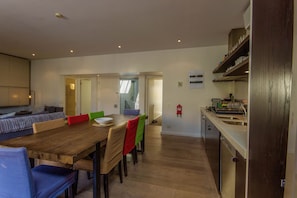 Un comedor amplio con una mesa y sillas de madera, una cocina con un lavamanos de acero inoxidable y un extintor visible en la pared.